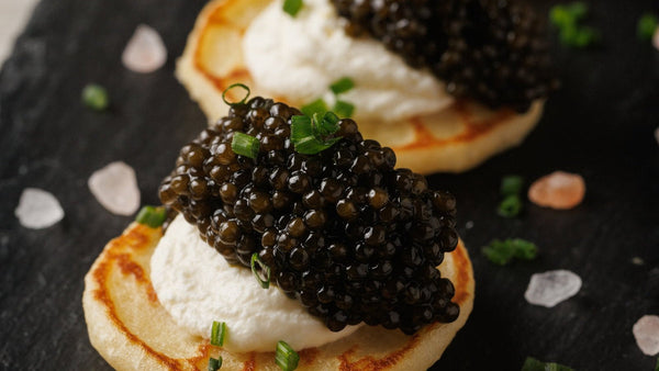 A pile of warm blinis on a small plate beside an open tin of caviar, the classic accompaniment for a caviar service.