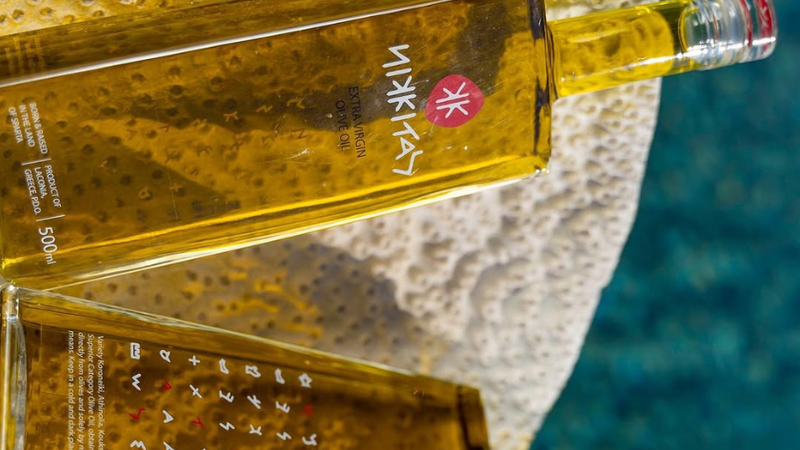 Close-up of golden extra virgin olive oil flowing from a dark bottle into a white ceramic bowl